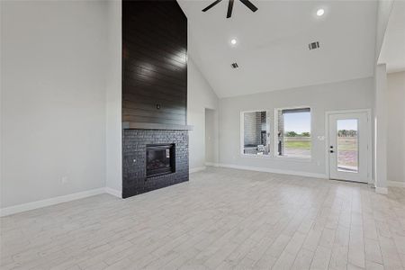 Unfurnished living room featuring ceiling fan, high vaulted ceiling, light wood-type flooring, and a brick fireplace