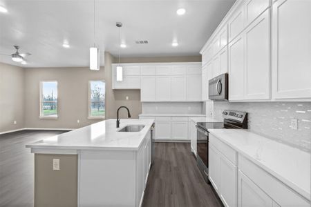 Kitchen with hanging light fixtures, appliances with stainless steel finishes, light stone countertops, a kitchen island with sink, and white cabinets