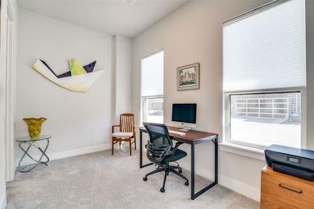 The first room off the foyer is a spacious study with light color carpeting and large windows with top-down, bottom up blinds.