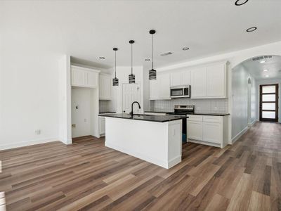 Kitchen featuring white cabinetry, hardwood / wood-style floors, stainless steel appliances, and a center island with sink