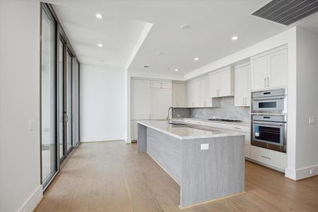 Open gourmet kitchen, where sleek custom cabinetry and beautiful countertops surround upscale appliances by Thermador and Sub-Zero. Floor to ceiling glass sliding doors open up to the blacony.