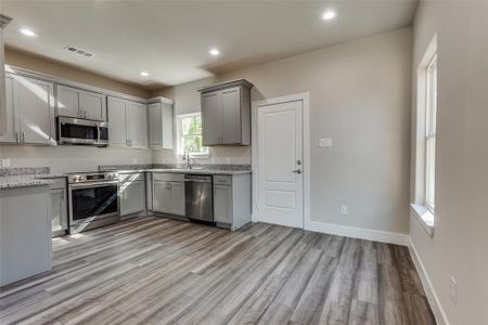 Kitchen featuring appliances with stainless steel finishes, light wood-style floors, gray cabinetry, and a sink