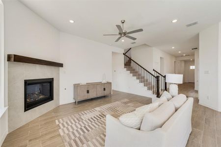 Living room with a tiled fireplace, ceiling fan, and light hardwood / wood-style flooring