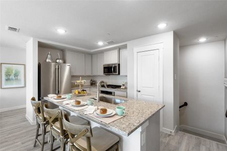 Kitchen with gray cabinetry, light hardwood / wood-style flooring, stainless steel appliances, an island with sink, and a breakfast bar area