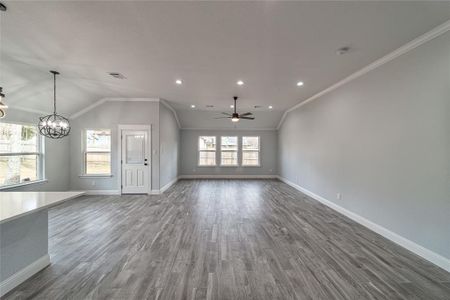 Unfurnished living room with baseboards, visible vents, ornamental molding, wood finished floors, and ceiling fan with notable chandelier