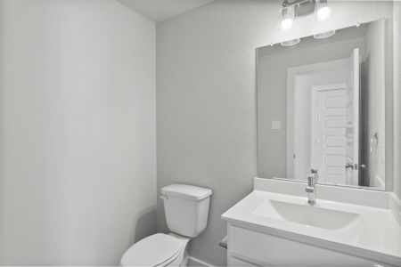 Sophisticated half bathroom adorned with contemporary finishes. The elegant 5-panel door welcomes you to a space where style meets functionality. Notice the sleek hardware accents that add a touch of modern charm. The vanity boasts light-colored countertops, beautifully complemented by a tasteful vanity light, creating a well-lit and inviting atmosphere. Sample photo of completed home with similar floor plan. As-built interior colors and selections may vary.