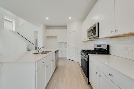 Kitchen with stainless steel appliances, sink, a center island with sink, light hardwood / wood-style flooring, and white cabinets