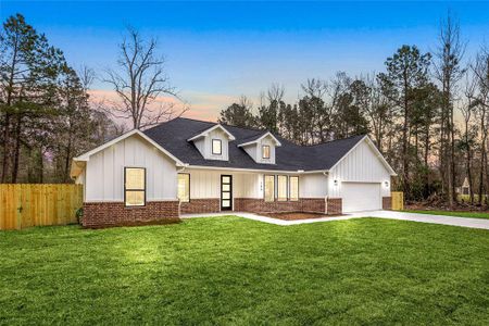 This charming home features a modern farmhouse design with a combination of white siding and brick accents. It has a spacious front yard, a two-car garage, and is surrounded by mature trees, providing a serene and private setting.