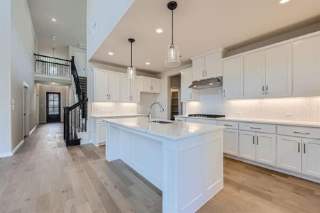 Kitchen featuring stainless steel gas cooktop, an island with sink, sink, white cabinetry, and light hardwood / wood-style floors