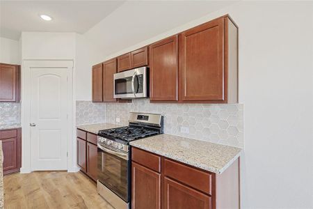 Kitchen with light stone countertops, decorative backsplash, light hardwood / wood-style floors, and appliances with stainless steel finishes