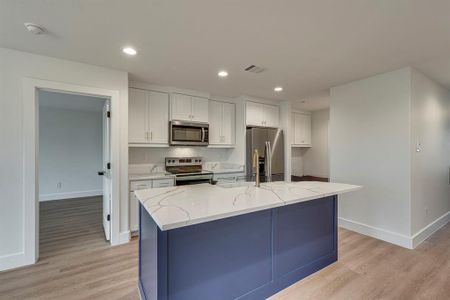 Kitchen with appliances with stainless steel finishes, visible vents, light wood-style floors, and white cabinetry