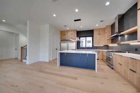 Kitchen with sink, a center island, light hardwood / wood-style floors, decorative light fixtures, and high end appliances