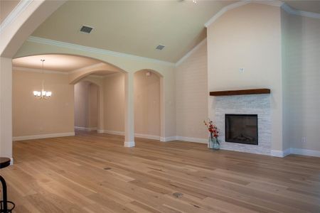 Unfurnished living room with lofted ceiling, a stone fireplace, light hardwood / wood-style flooring, ornamental molding, and a chandelier