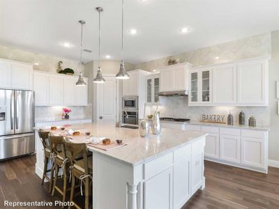 Kitchen with dark hardwood / wood-style flooring, stainless steel appliances, hanging light fixtures, and an island with sink