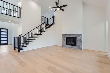 Unfurnished living room with a tile fireplace, ceiling fan, light hardwood / wood-style flooring, and a high ceiling