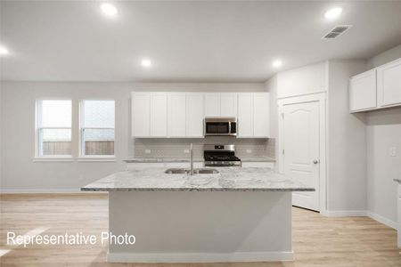 Kitchen with light stone countertops, sink, white cabinetry, stainless steel appliances, and a kitchen island with sink