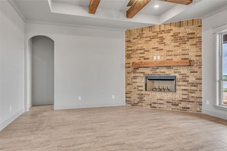 Unfurnished living room featuring light hardwood / wood-style flooring, ceiling fan, beamed ceiling, and a fireplace