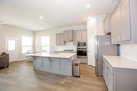 Kitchen with a center island with sink, sink, a kitchen breakfast bar, gray cabinets, and appliances with stainless steel finishes