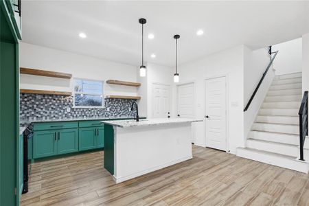 Kitchen featuring decorative light fixtures, light stone counters, a center island with sink, tasteful backsplash, and sink