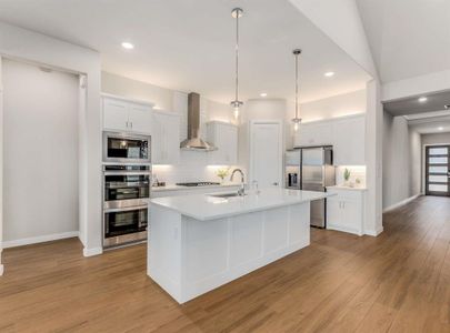 Gourmet chef’s kitchen boasts white cabinetry with under and above-cabinet lighting, a large island, quartz countertops, subway tile backsplash, and stainless-steel appliances, including a 5-burner gas cooktop and double convection ovens