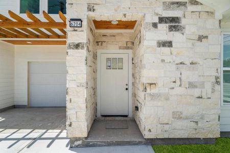 This home features a modern exterior with a stone facade entryway, a single-car garage, and a wooden pergola overhang, offering a blend of traditional charm and contemporary design.