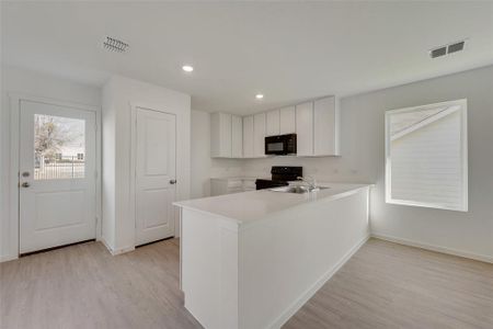 Kitchen with white cabinets, black appliances, sink, kitchen peninsula, and light hardwood / wood-style flooring