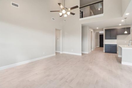 Unfurnished living room with ceiling fan, sink, a high ceiling, and light hardwood / wood-style flooring