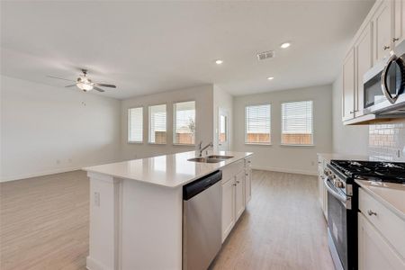 Kitchen with appliances with stainless steel finishes, light hardwood / wood-style floors, white cabinetry, a kitchen island with sink, and sink