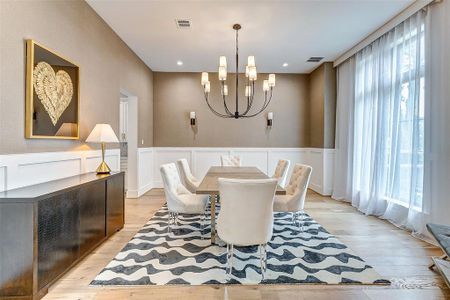 This elegant dining room features a modern chandelier, neutral tones, and ample natural light from large windows. The space includes a long table with plush chairs, a stylish sideboard, and a decorative rug, creating a sophisticated and inviting atmosphere.