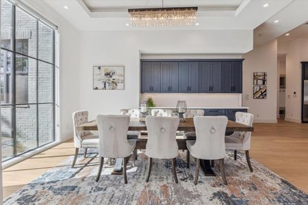 This formal dining room features a spacious layout with a large window offering natural light and views of the outdoors. The coffered ceiling adds depth and elegance, complemented by recessed lighting and a central chandelier for ambiance. Along the back wall, built-in navy cabinetry with sleek hardware provides ample storage and a polished backdrop. The light wood flooring ties the space together, creating a warm and inviting atmosphere.