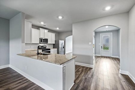 Kitchen featuring dark wood-style floors, arched walkways, appliances with stainless steel finishes, a sink, and light stone countertops