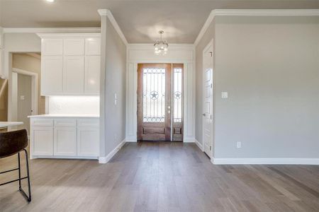 Entrance foyer with ornamental molding, an inviting chandelier, and light hardwood / wood-style flooring