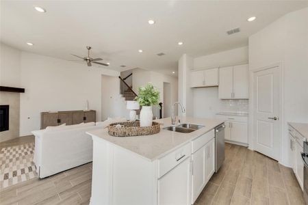 Kitchen with sink, an island with sink, white cabinetry, a fireplace, and ceiling fan