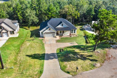 The aerial view of this home features a gable roof and an attached two-car garage, nestled among mature trees with a spacious driveway and a sizable front yard, offering privacy and a serene environment.