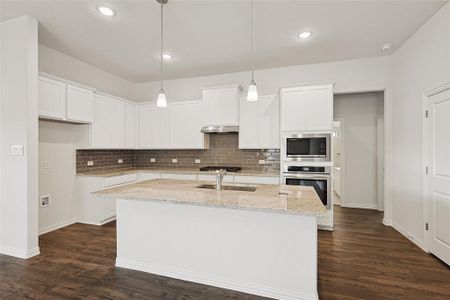 Kitchen with dark hardwood / wood-style flooring, appliances with stainless steel finishes, white cabinetry, and an island with sink