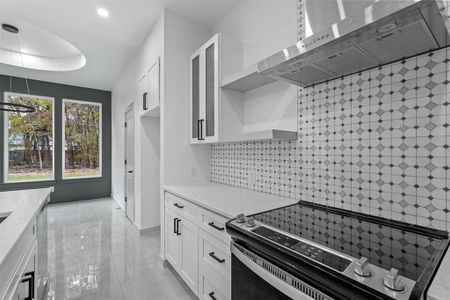 Kitchen with light stone countertops, stainless steel appliances, tasteful backsplash, range hood, and white cabinets