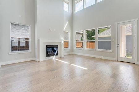 Unfurnished living room featuring light hardwood / wood-style flooring, a healthy amount of sunlight, and a towering ceiling