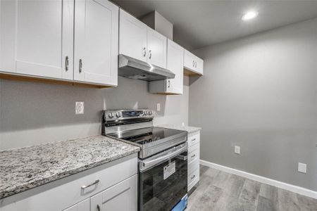 Kitchen with stainless steel electric stove, white cabinets, light wood-type flooring, and light stone counters