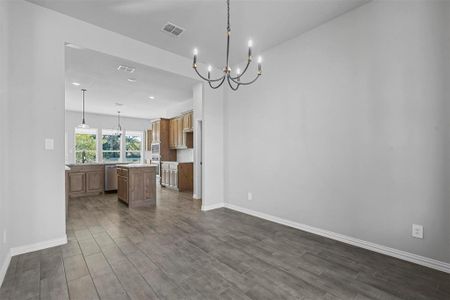 Kitchen with an inviting chandelier, decorative light fixtures, a center island, stainless steel dishwasher, and hardwood / wood-style flooring