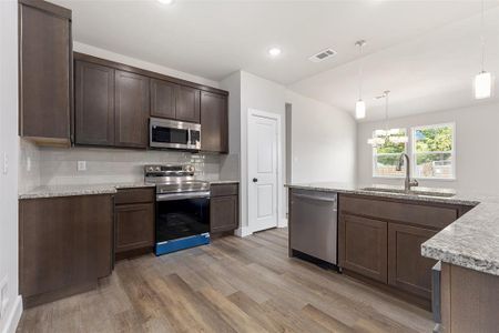 Kitchen featuring decorative backsplash, appliances with stainless steel finishes, dark brown cabinets, pendant lighting, and light wood-type flooring