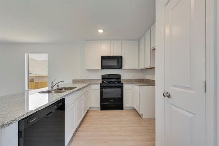 Kitchen featuring black appliances, sink, light hardwood / wood-style floors, light stone countertops, and white cabinetry