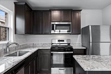 Kitchen featuring sink, light stone counters, stainless steel appliances, and dark brown cabinets