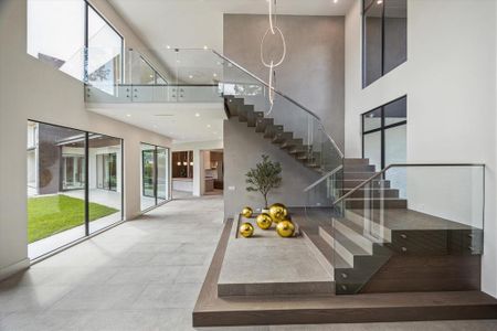 Upon entry through the custom steel door, you're greeted by a double-height foyer with expansive windows offering stunning views of the front lawn. The dune-carved natural floor tile sets a serene tone, while floating white oak and steel stairs with glass railings lead to the second floor. An inclination elevator provides seamless access upstairs, complemented by designer-neutral wall paint and recessed LED lighting.