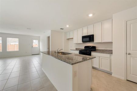 Kitchen featuring dark stone countertops, sink, black appliances, white cabinets, and an island with sink