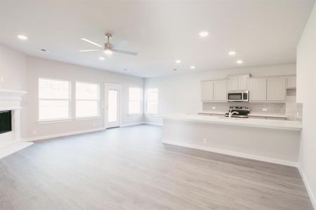 Kitchen with light wood-type flooring, ceiling fan, stainless steel appliances, white cabinets, and tasteful backsplash