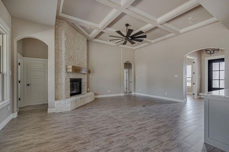 Unfurnished living room with beamed ceiling, coffered ceiling, ceiling fan, a stone fireplace, and hardwood / wood-style flooring