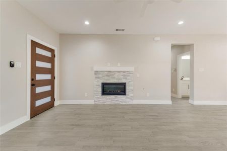 Unfurnished living room with a stone fireplace, ceiling fan, and light hardwood / wood-style flooring