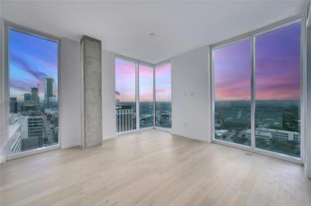 Stunning Corner Living Room with Panoramic City Views. This modern corner living room offers breathtaking panoramic views of the Austin skyline through floor-to-ceiling windows. The spacious, open layout is bathed in natural light, creating a bright and airy atmosphere perfect for both relaxation and entertaining. The light wood flooring adds warmth to the contemporary design, while the exposed concrete pillar adds a touch of urban sophistication. Watch the sunset over the city and enjoy the vibrant colors of the sky from the comfort of your own home. *Linden Residence No. 2105 Shown Here