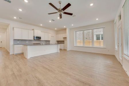 Kitchen featuring ceiling fan, decorative backsplash, light wood-type flooring, white cabinets, and an island with sink