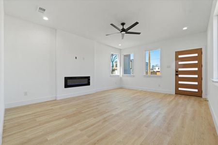 Unfurnished living room featuring a ceiling fan, baseboards, visible vents, light wood-style floors, and a glass covered fireplace